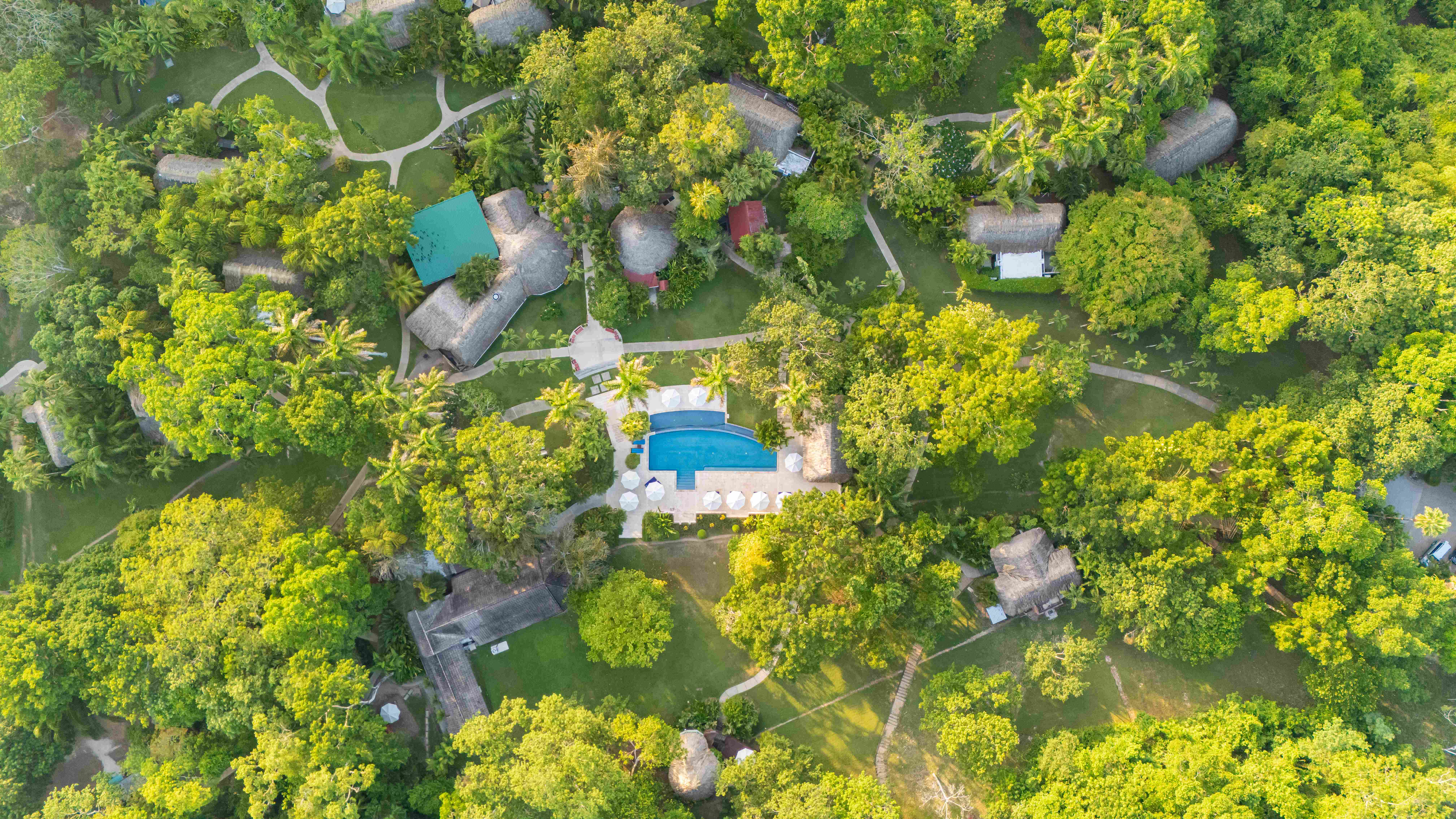 Luxury eco‑resort aerial view with pool and jungle trails at The Lodge at Chaa Creek, Belize Aerial view of jungle eco‑resort with pool and network of thatched cottages at The Lodge at Chaa Creek, Belize