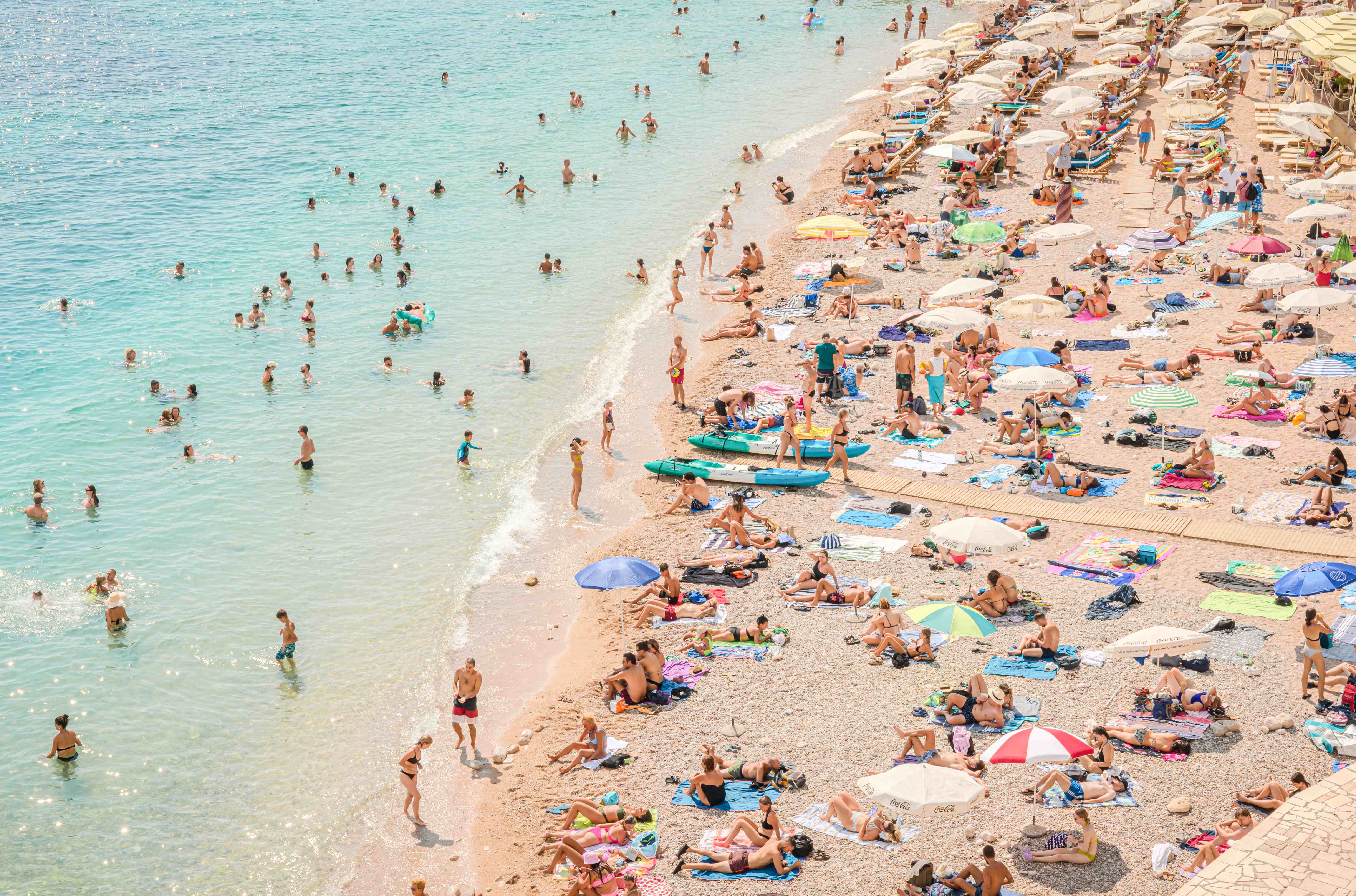 Lively summer beach scene at Banje Beach in Dubrovnik, Croatia Crowded summer beach scene at Banje Beach with umbrellas and turquoise water in Dubrovnik, Croatia