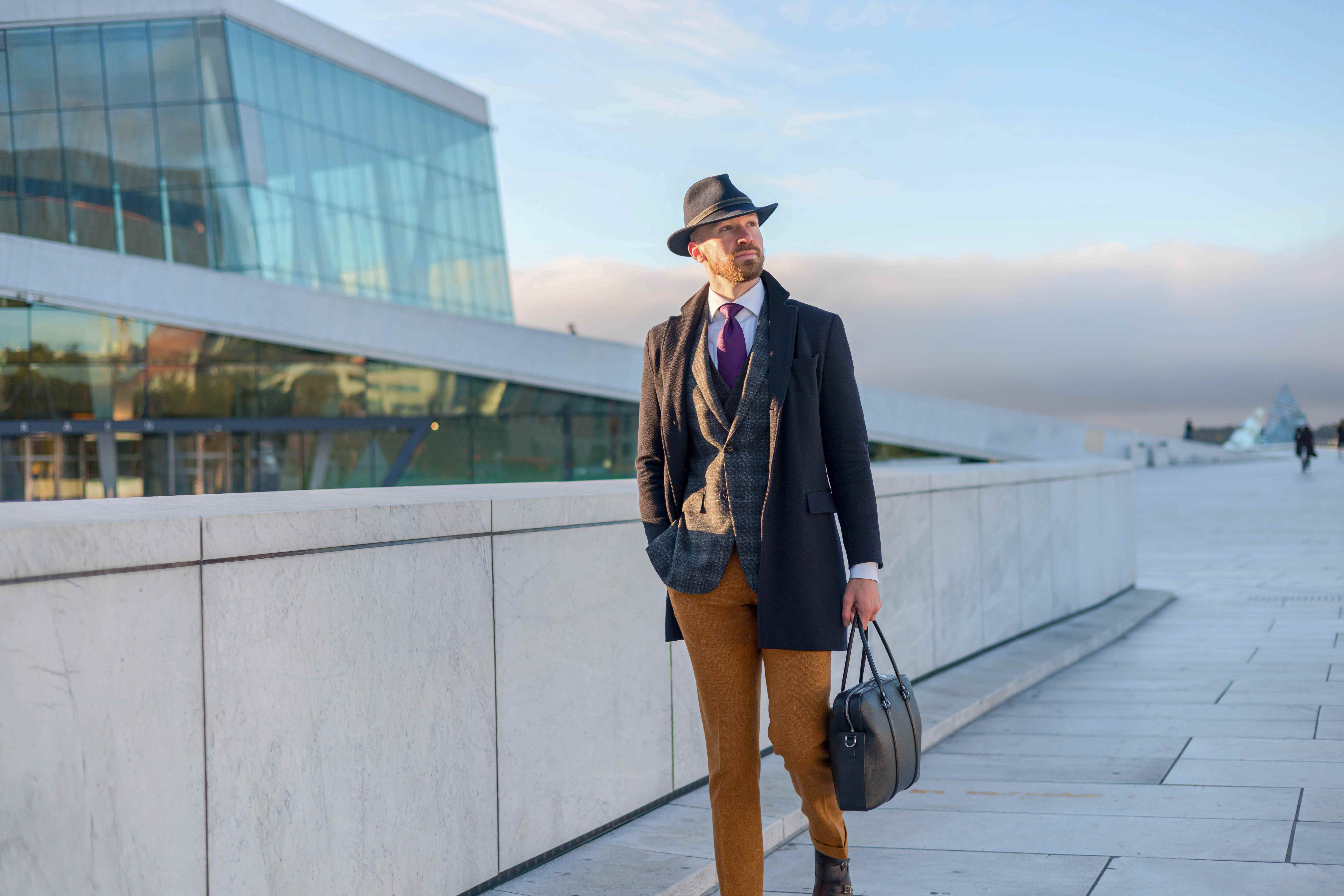 Businessman in stylish fedora walks past Oslo Opera House exterior walkway Man in stylish business attire walking near Oslo Opera House with briefcase