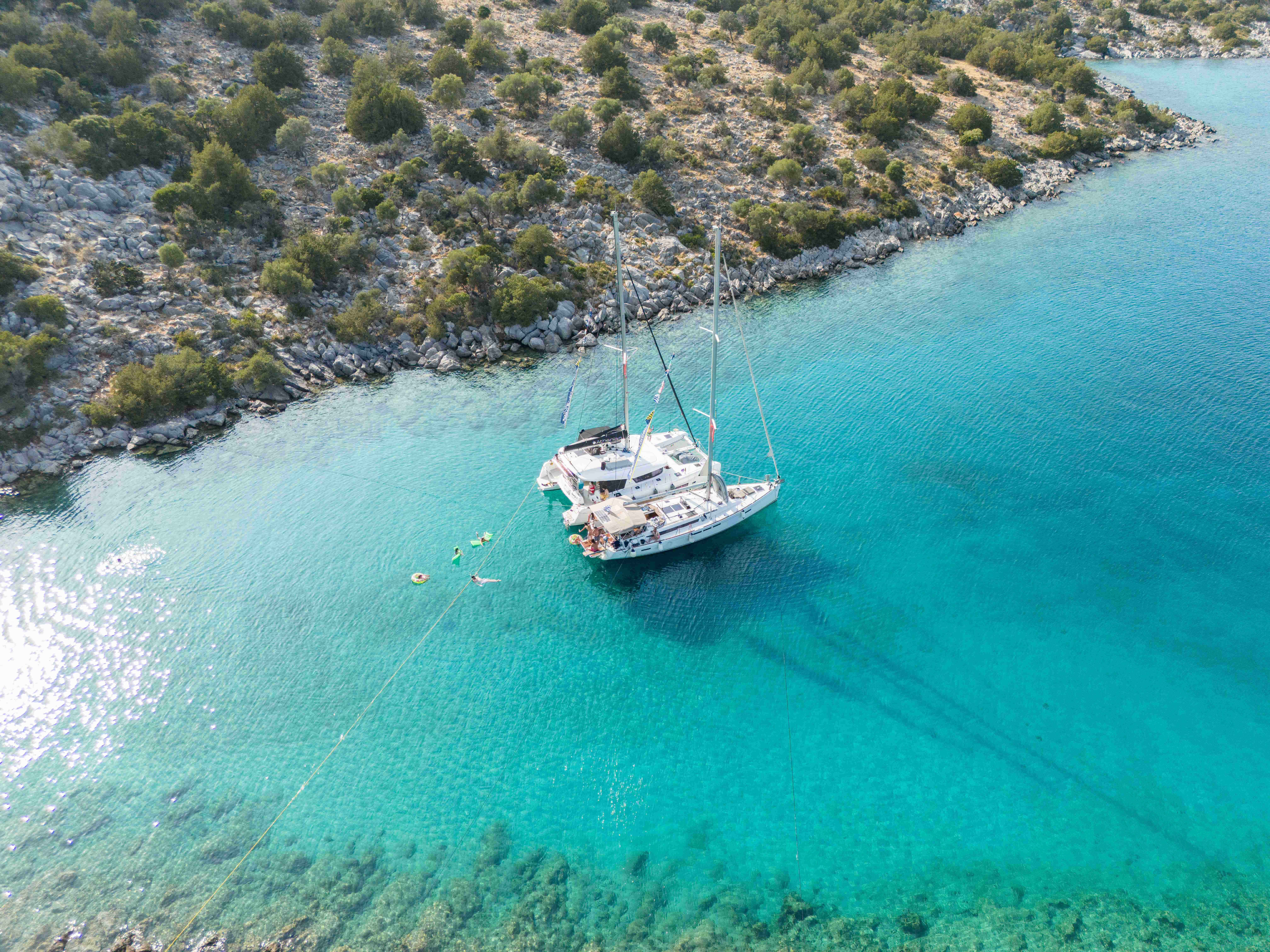 Aerial side view of a catamaran and monohull sailboat with people relaxing in Mediterranean waters in Greece Aerial side view of a catamaran and sailboat with people relaxing in turquoise waters in Greece
