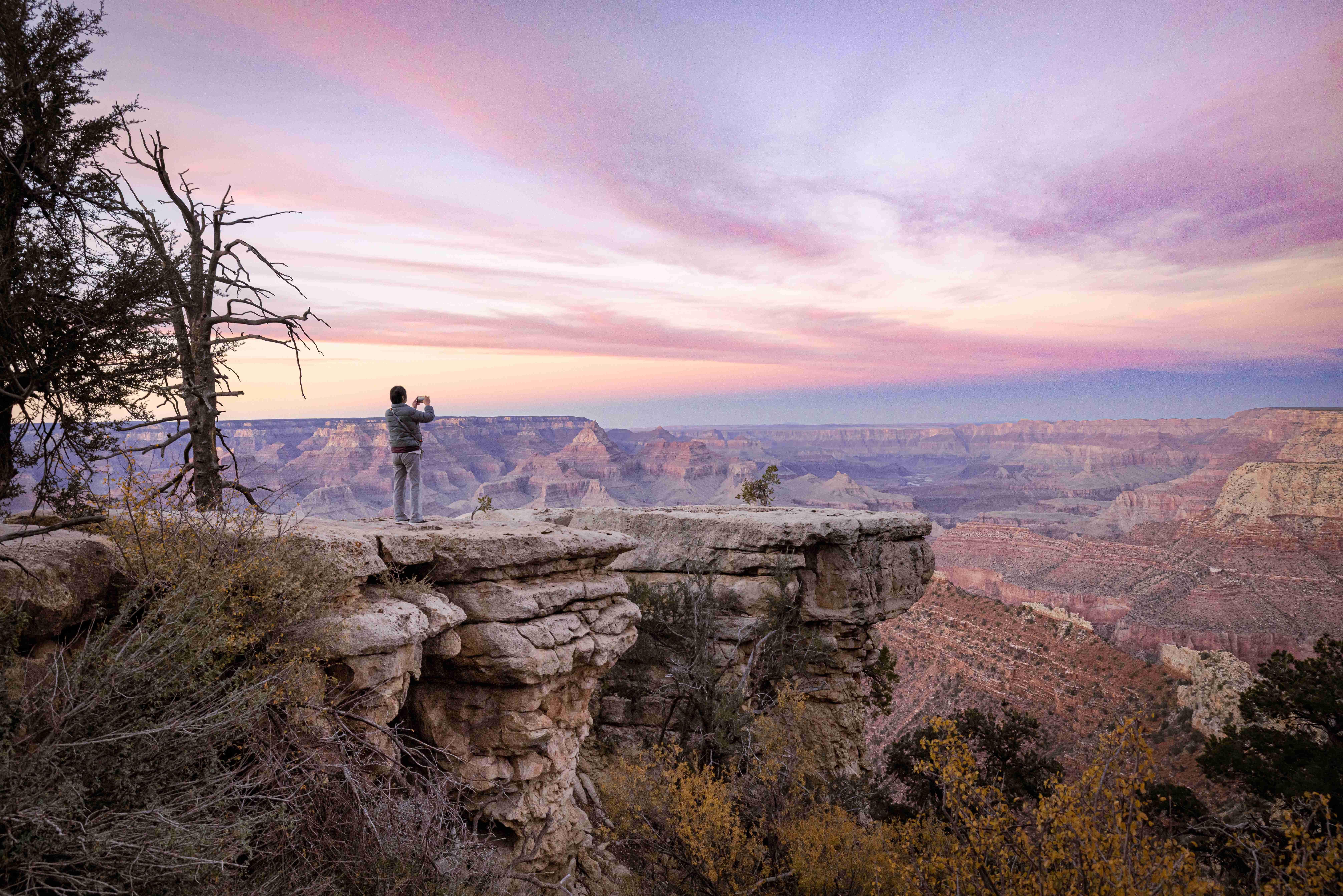 Tourist photographing Grand Canyon South Rim at dusk under colorful sky Tourist taking photo at Grand Canyon South Rim at dusk with colorful sky