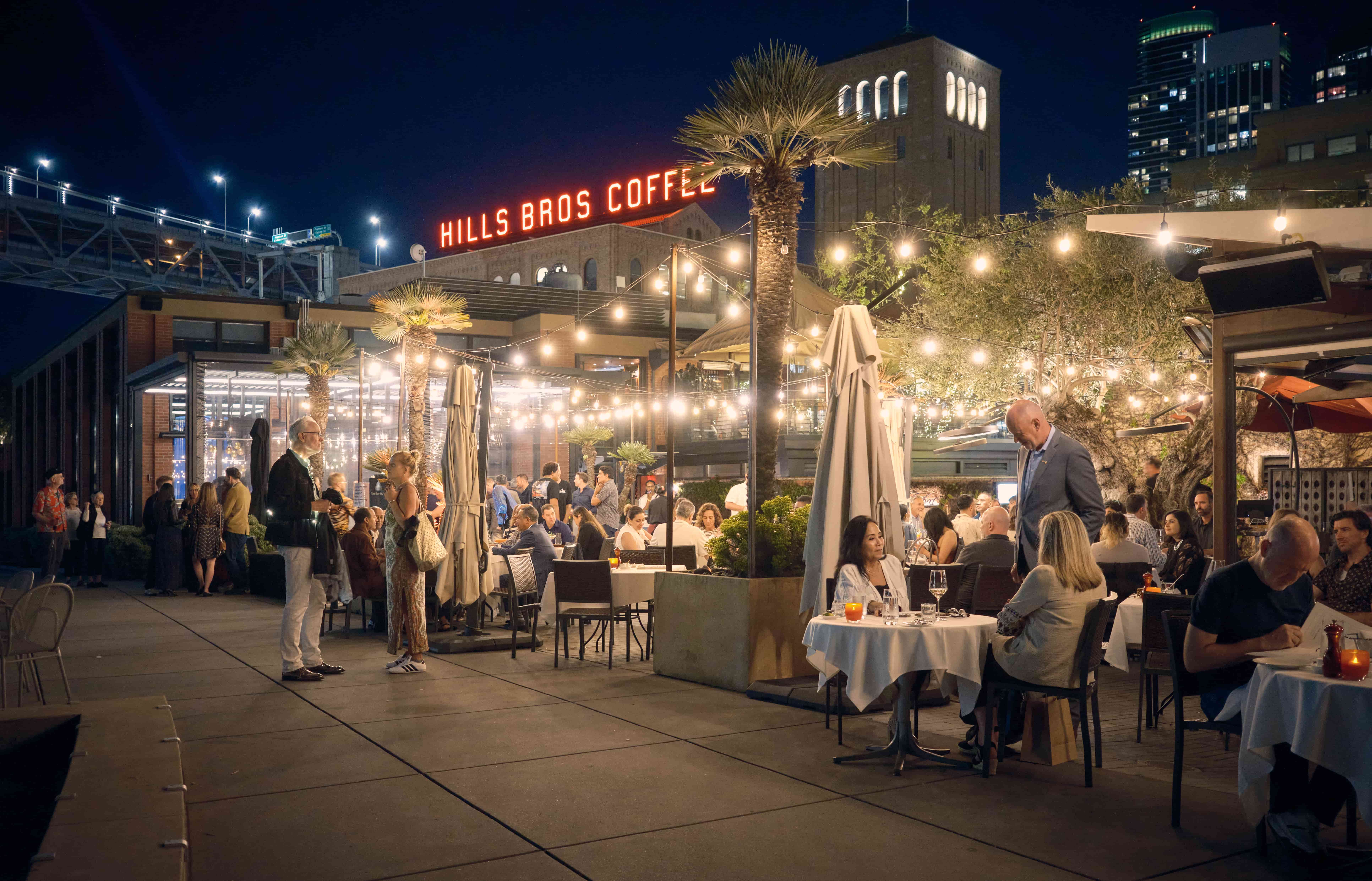 Lively evening dining at Waterbar on the Embarcadero, San Francisco Outdoor evening dining on Waterbar patio with Hills Bros Coffee sign behind