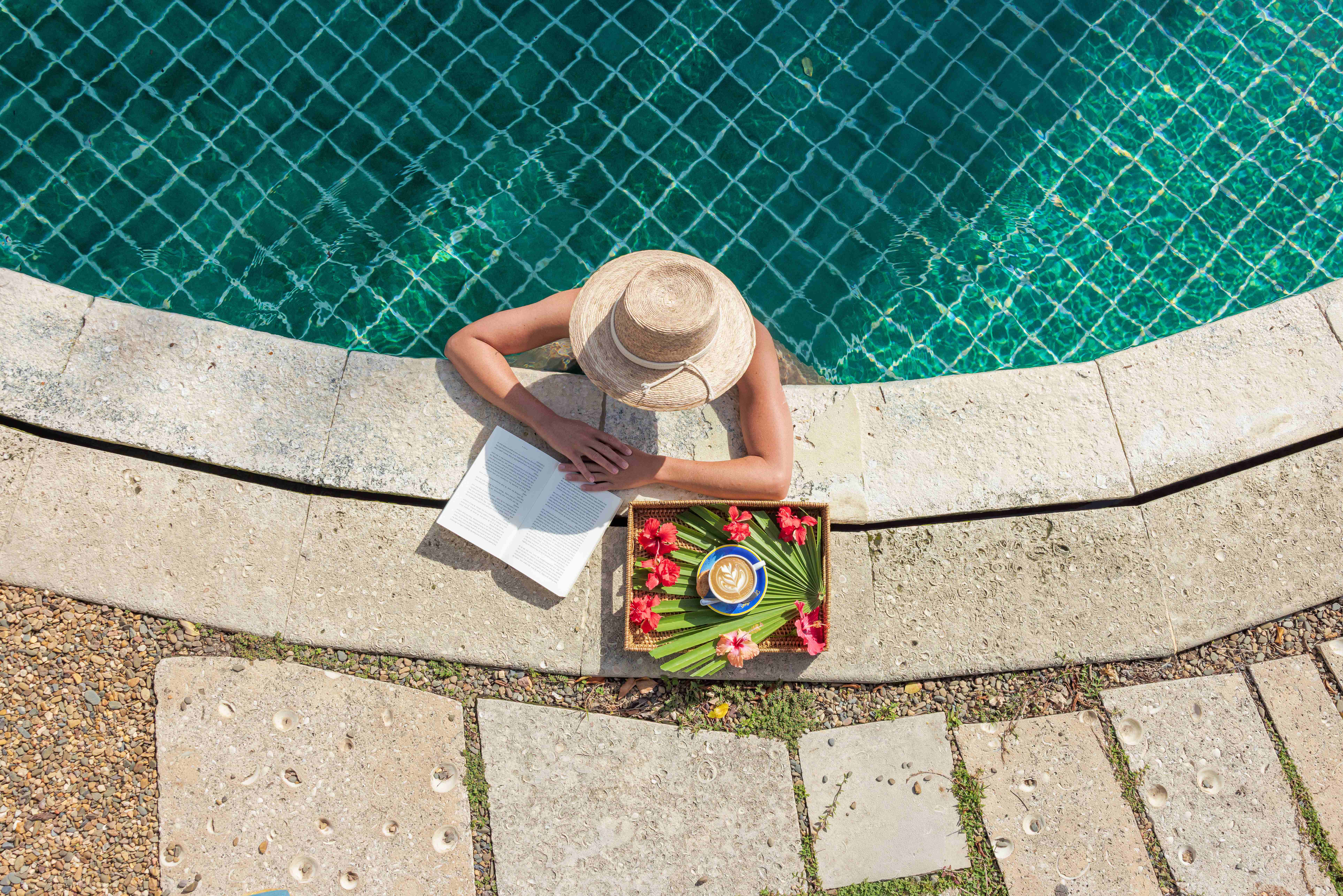 Woman relaxing with latte and book at upscale resort pool in Belize Woman reading a book beside a resort pool in Belize with a tray holding a latte and tropical flowers