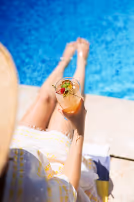 Woman relaxing poolside with tropical cocktail at luxury resort in Belize Close-up of a woman in a sundress holding a tropical cocktail while relaxing beside a swimming pool at a luxury resort